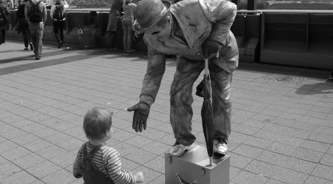 Hier sieht man einen Straßenkünstler, der einem sehr kleinen Jungen die Hand reicht