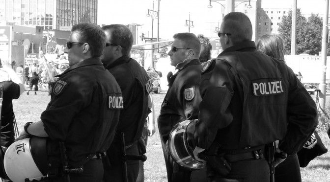 Hier ist ein Bild mehrerer Polizisten bei einer Demonstration zu sehen. Die Gesichter sind nicht erkennbar, die Beamten stehen der Kamera abgewandt