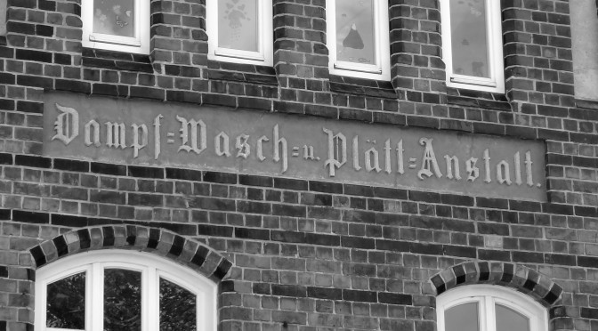 Hier ist ein Bild aus Wismar zu sehen, eine geklinkerte Hausfassade (Backstein-Gothik) mit einer alten, eingemeißelten Schrift. Die Inschrift lautet: "Dampf- Wasch und Plättanstalt"