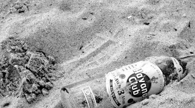Hier ist eine leere Flasche Rum im Sand eines Strandes zu sehen