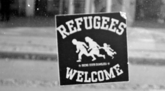 Hier sieht man einen Aufkleber auf einer Straßenbahnhaltestelle, der Text lautet "Refugees welcome"