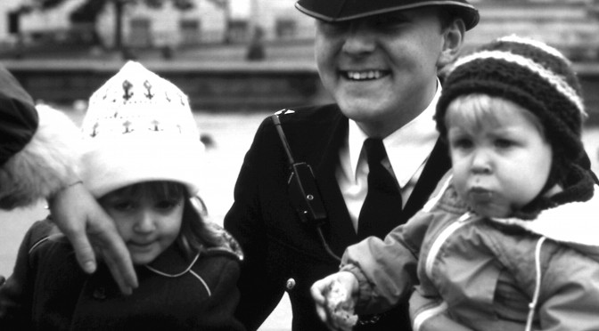 Mein Bruder und ich als ganz kleine Kinder auf dem Schoß eines englischen Bobbys, eines Polizisten. Links im Bild die Hand meiner Mutter, die meine Wange streichelt.