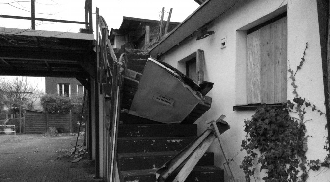 Hier ist ein Bild von einem heruntergekommenen Haus mit einer Freitreppe aufs Dach zu sehen. Die Absperrung mit einem "Zutritt verboten" Schild ist eingetreten.