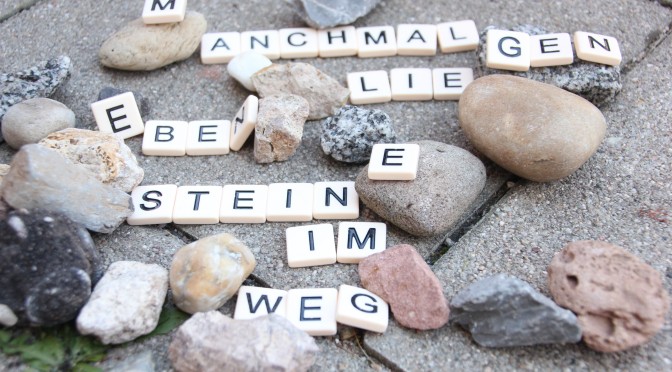 Hier sieht man Buchstaben auf Steinen, die einen Spruch ergeben. Der Spruch lautet "manchmal liegen eben Steine im Weg"